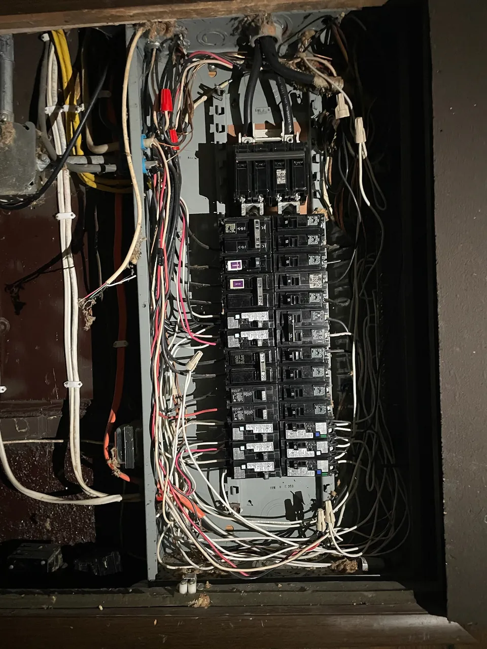 Old electrical panel with the cover removed, showing tangled wiring before replacement